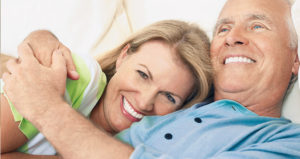 Retired couple with new dental implants smile while embracing in bed